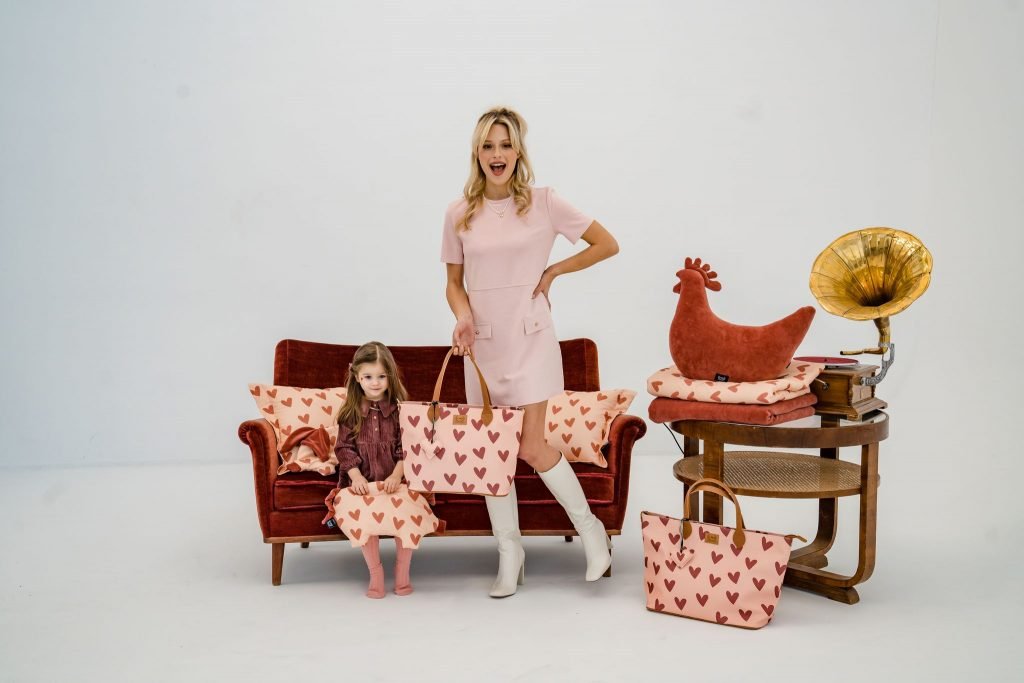 Heartbeat Cotto Sleepy Pig Pink, το οποίο κρατάει στο χέρι του ένα παιδάκι με διάφορα προϊόντα της συλλογής Heartbeat γύρω της